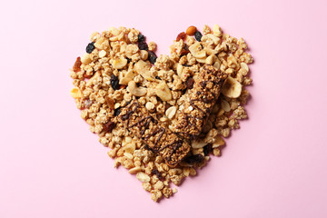 Heart made of healthy granola bars and ingredients on pink background, flat lay
