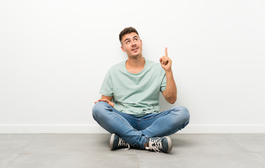 Young handsome man sitting on the floor pointing with the index finger a great idea