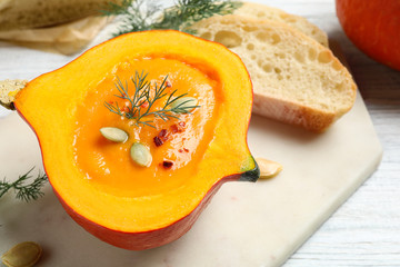Tasty cream soup in pumpkin half on white wooden table, closeup