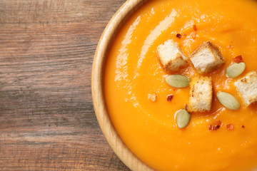 Bowl with tasty pumpkin cream soup on wooden table, top view. Space for text