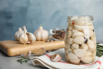 Composition with jar of pickled garlic on grey table against blue background. Space for text