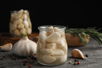 Composition with jar of pickled garlic on grey table against black background