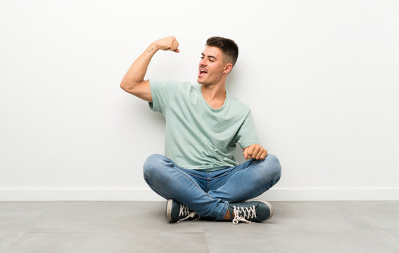 Young Handsome Man Sitting On The Floor Making Strong Gesture