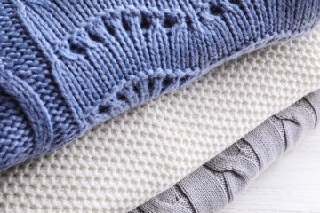 Stack of soft knitted sweaters on table, closeup