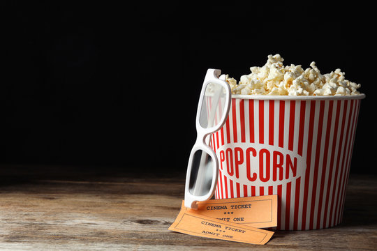 Popcorn, cinema tickets and 3d glasses on wooden table against black background. Space for text
