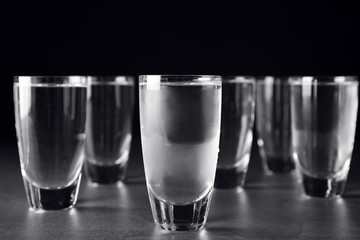 Shots of vodka on grey table against black background