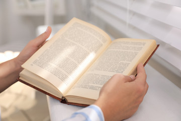 Fototapeta premium Woman reading book near window at home, closeup
