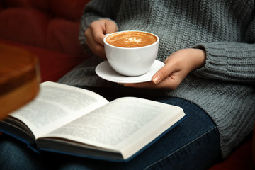 Woman with cup of coffee reading book on sofa, closeup