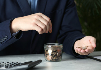 Fototapeta na wymiar Man putting coin into jar at grey marble table, closeup. Money savings