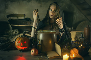 Fototapeta na wymiar Beautiful witch in black mantle with a pumpkin and magical things on Halloween celebration