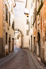 Fototapeta na wymiar Narrow street with gate, tower in Rovereto, Italy