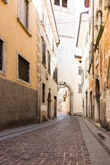 Fototapeta na wymiar small street with brown orange houses and civil tower, gate. Rovereto, Italy