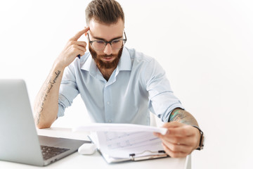 Image of man in eyeglasses working on laptop and documents in office