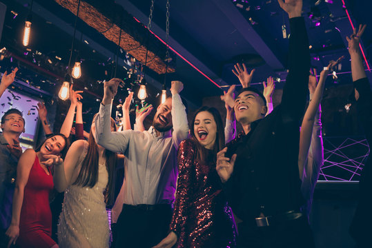 Photo of excited cheerful beautiful well dressed company corporate dressed in formalwear dancing with their hands up at night club confetti falling neon lights shining