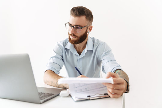 Image of man in eyeglasses working on laptop with documents in office