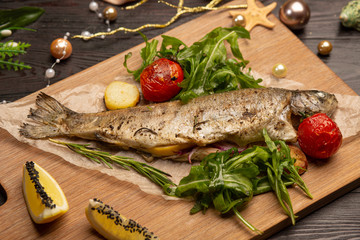 fried trout with arugula, cherry tomatoes and lemon on a board