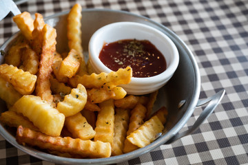 Close up of tasty french fries in bowl with ketchup on tartan table background.