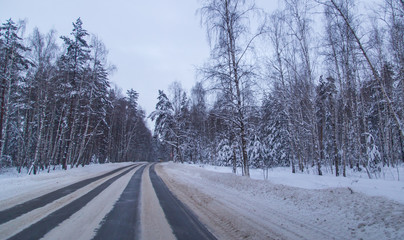Obraz na płótnie Canvas Asphalt road in the forest covered with snow