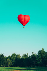 Red hot air balloon in the shape of a heart against the blue sky and some light clouds. Concept of love and peace.