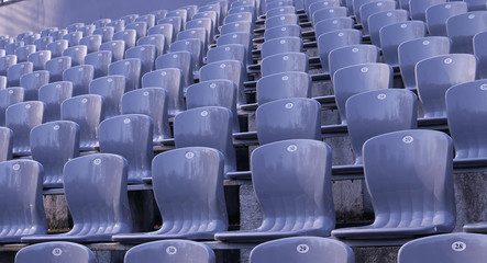  Gray stands in an empty stadium on a sunny day. Style and precision. Gray seats with numbers.