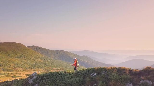 Tourist hiker with a backpack in orange jacket walking on mountain path in Carpathian mountains.