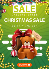 Special offer, Christmas sale, up to 50% off, green vertical banner with Christmas tree branches, garlands, button and present with Teddy bear