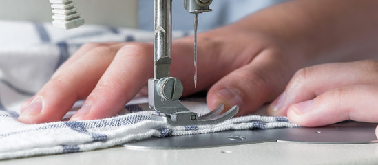 Hands of a girl sews on a white sewing machine close-up on a blue background with copy space...