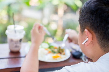 Selective focus to the boy was happily eating a salad and wearing a wireless headset.
