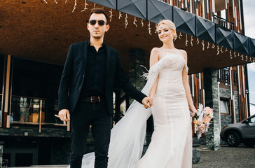 Naklejka premium Stylish wedding couple. Young woman in white wedding dress and jewelry tiara with veil. Groom in a black suit.