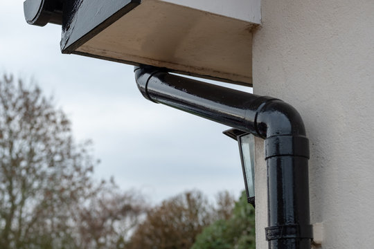 Detailed view of a newly painted gutter and down pipe drainage system seen together with part of a security lantern at the porch of a large house during winter.