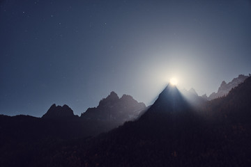 The moon rises from behind the mountains. Mountain night landscape. Alps, Chamonix, France.