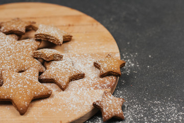  Star-shaped gingerbread cookie sprinkled with icing sugar on a wooden round cutting board.