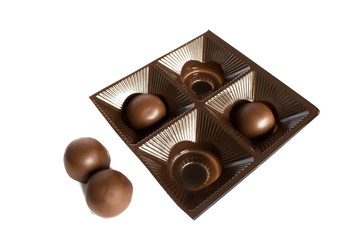 Two round chocolate candies in a plastic square package and two next to it on a white background