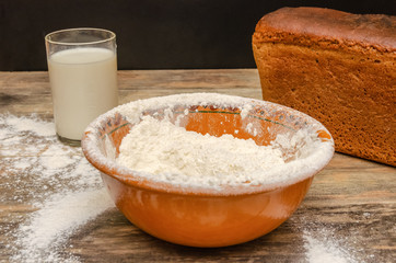 Fresh bread brick on the table closeup. Next is a bowl of flour, a glass of milk