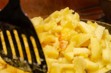 woman's hand with a black spatula stirs potatoes while frying in a frying pan close up