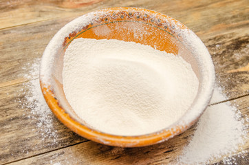 Flour in a ceramic brown bowl with a row of scattered flour on a wooden background close-up. The view from the top