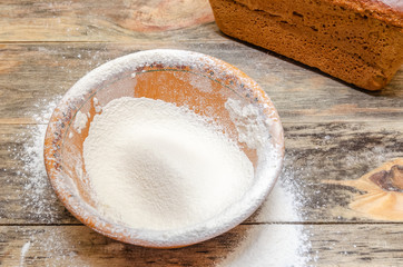 bowl of flour, egg, milk is on a wooden table, next to a loaf of bread. The concept of baking bread.