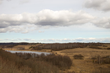 Fototapeta na wymiar Panorama of the spring landscape with a lake and hills with copses. Izborsk, Pskov region, Russia.