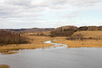 Panorama of the spring landscape with a lake and hills with copses. Izborsk, Pskov region, Russia.