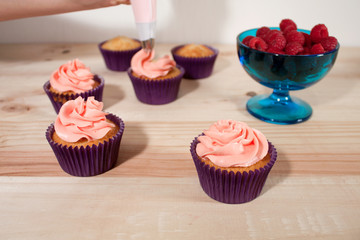 Frosting vanilla and raspberry cupcakes on wood table