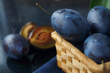 Fresh juicy plums in basket on black metal background with reflection