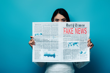 asian woman in white blouse holding newspaper with fake news on blue background