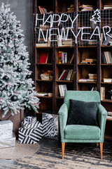 Cozy corner of the living room with a bookcase and a mint chair next to a Christmas tree dressed in black toys and gift boxes with inscription Happy New Year. Concept of Christmas Eve and festive mood