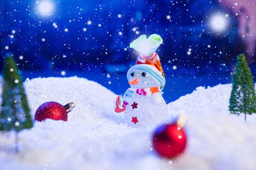 Snowman with Christmas balls on snow over fir-tree, night sky and moon. Shallow depth of field. Christmas background. Fairy tale. Macro. Artificial magic dreamy world.