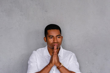 Young desperate ethnic young male businessman praying bowing his head and posing on a gray background. Concept of failures and black stripe in life. Advertising space