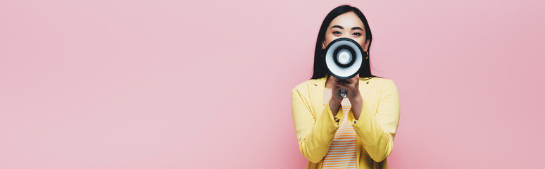Fototapeta premium asian woman in yellow outfit holding megaphone isolated on pink, panoramic shot