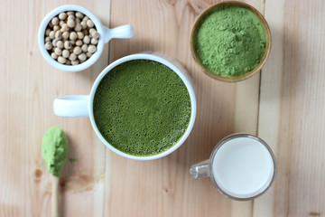 Top view, Closes up Hot Green Tea Matcha Latte on wooden board. Decorate with powder extract and soy beans and fresh milk.