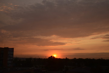 View of the dramatic sky above the sity at sunset with dark blue clouds and pink, purple and yellow flashes from the sun's rays