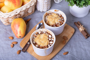 Crumble with caramelized pear, cinnamon and almonds in a white ramekin. Close-up.