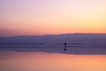 Photographer taking pictures of sunrise on the shore of the Dead Sea